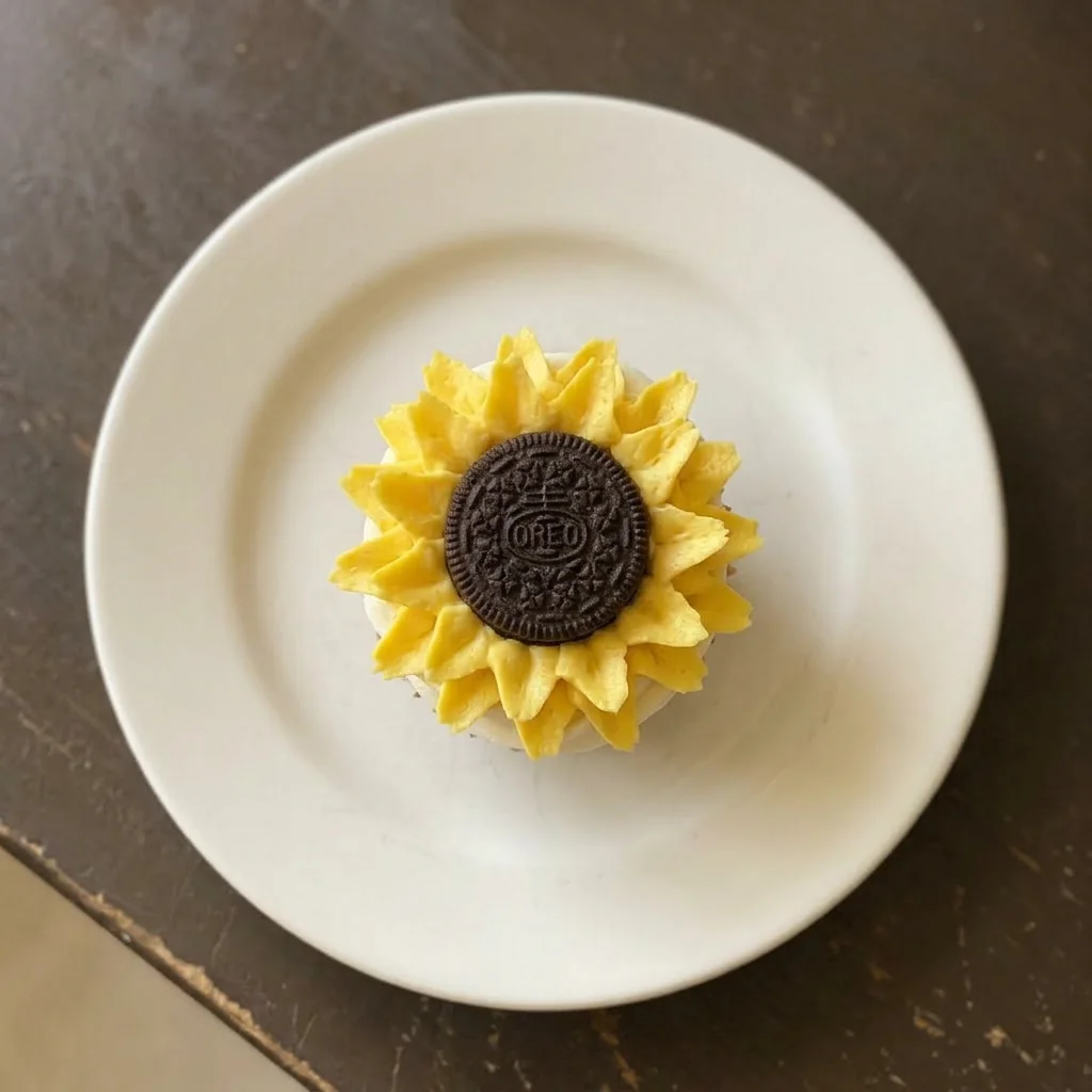 A plate of vanilla cupcakes with yellow buttercream, each topped with a whole Oreo cookie and crushed Oreo pieces.