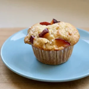 Top-down look at a plum muffin with a golden dome, a plum slice on top, and yogurt visible in the crumb.