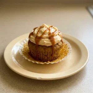 Overhead shot of a pumpkin cupcake topped with caramel cream cheese frosting, visible spices, and caramel drizzle.