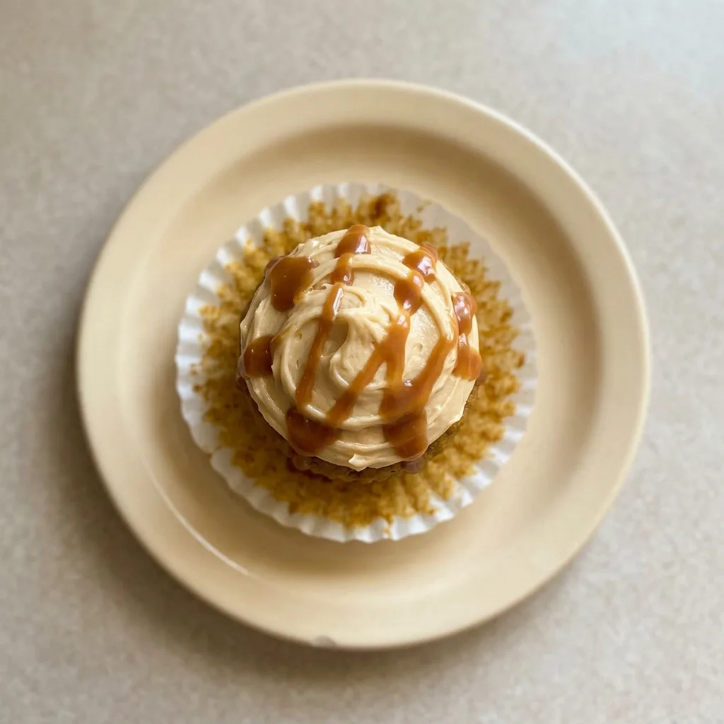 Plated pumpkin cupcake with caramel cream cheese frosting, garnished with a caramel candy and cinnamon stick.