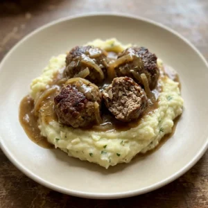 Bird's-eye view of three Salisbury steak meatballs with gravy on a bed of mashed potatoes, topped with parsley.