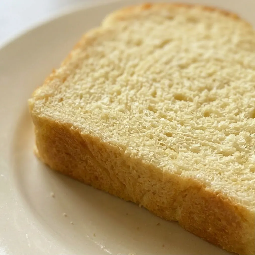 Macro detail of a slice of bread revealing a tender, pale crumb with small air pockets and a smear of melted butter.
