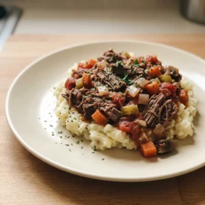 Bird's-eye view of shredded beef in dark sauce with mushrooms, carrots, and onions, topped with fresh herbs.