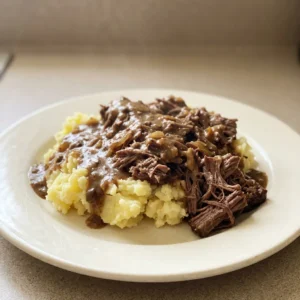 Top-down look at three beef short ribs in a glossy brown sauce with visible mushroom slices and onion flakes.