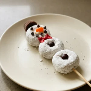 Top-down look at a skewer of mini donuts with peanut butter cups, chocolate chips, M&M's, and Mike & Ike candies on white frosting.