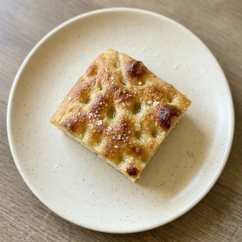 A serving of focaccia slice showing porous texture, browned edges, and scattered salt crystals.