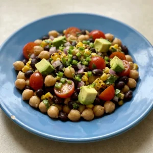 Bird's-eye view of a salad with chickpeas, black beans, corn, cherry tomatoes, red onion, jalapeno, cilantro, and avocado, seasoned with chili powder, cumin, and smoked paprika.