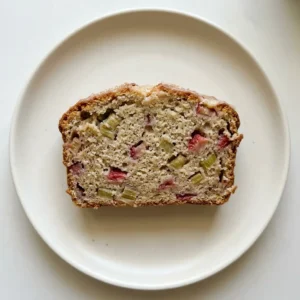 Bird's-eye view of a rectangular loaf topped with strawberry and rhubarb pieces, a yogurt glaze, and cinnamon specks.