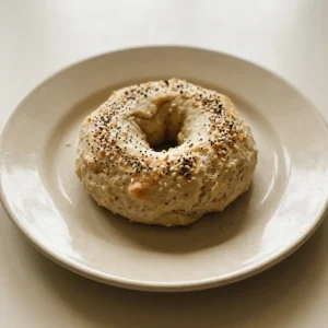 Overhead shot of two round bagels topped with Everything But the Bagel seasoning on a dark surface.