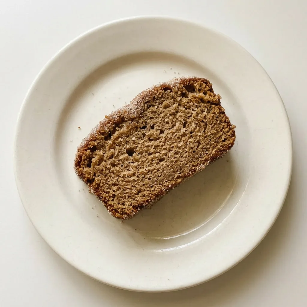 A serving of apple cider doughnut loaf cake, a thick slice with a buttery, spiced crust and a drizzle of glaze.