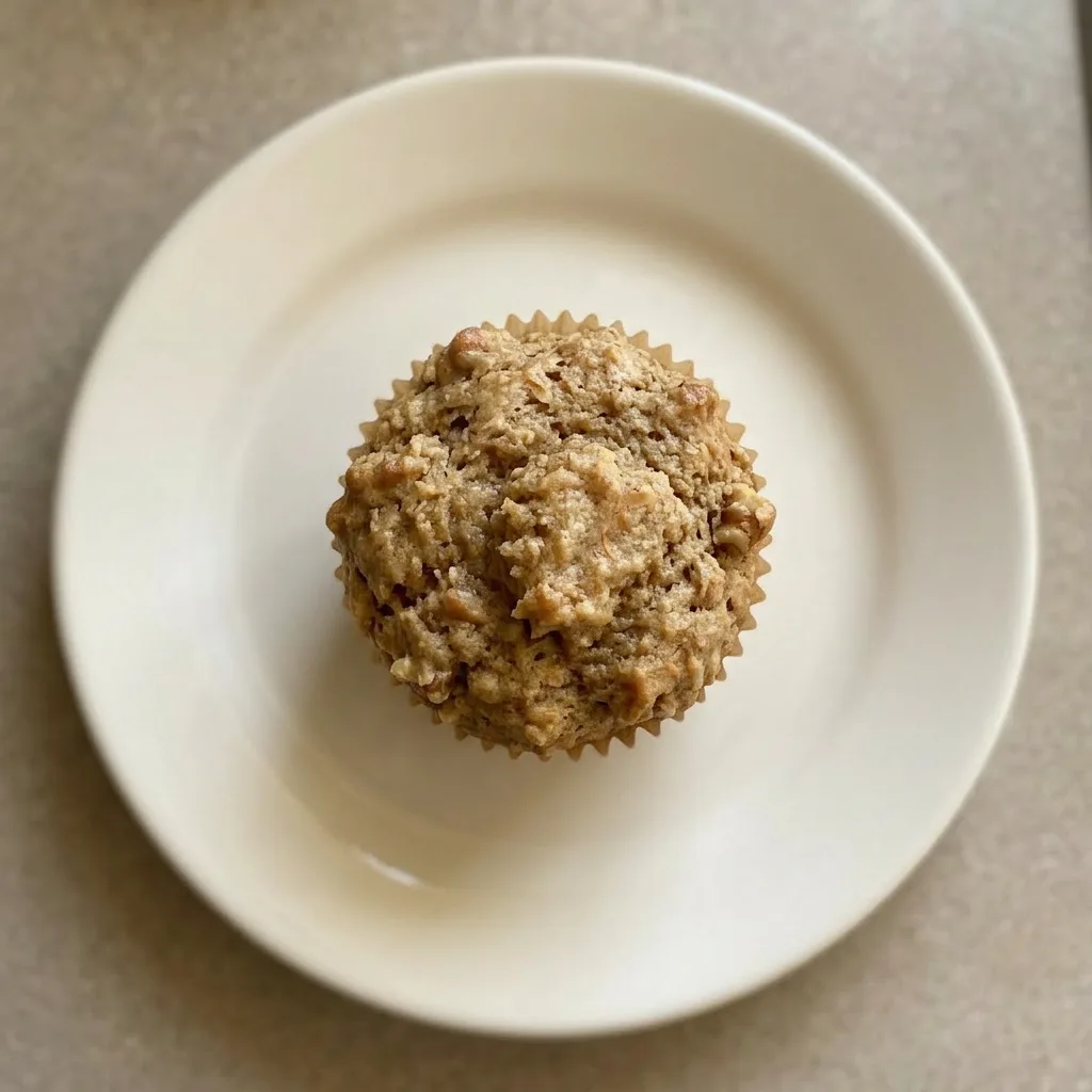 Plated muffin with a glossy top, studded with apple pieces and walnuts, cinnamon dusted.
