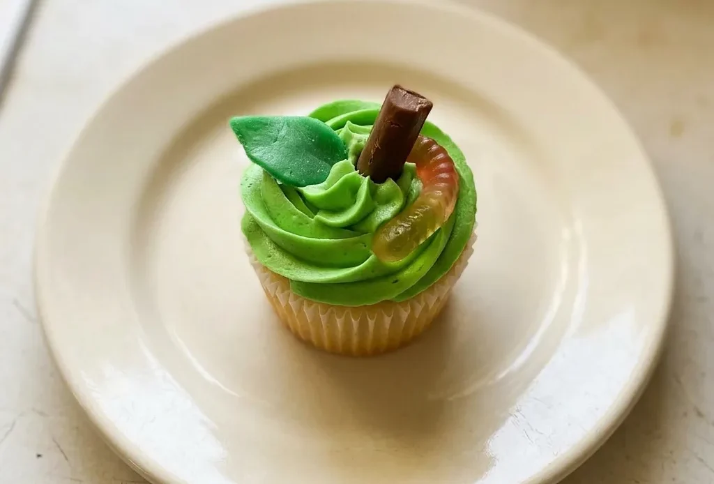 Overhead shot of a frosted apple cupcake topped with a Tootsie Roll, Airhead, and gummy worms.