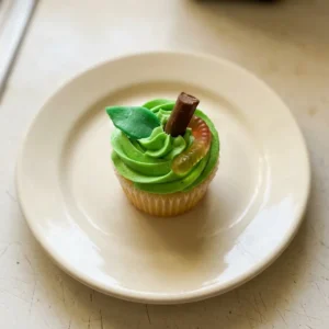 Overhead shot of a frosted apple cupcake topped with a Tootsie Roll, Airhead, and gummy worms.
