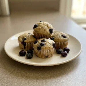 Top-down look at a round muffin with blueberries and banana slices on top, Greek yogurt visible in the batter.