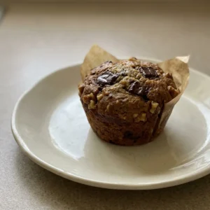 Looking down at three banana chocolate chunk muffins topped with walnut halves and dark chocolate chunks.