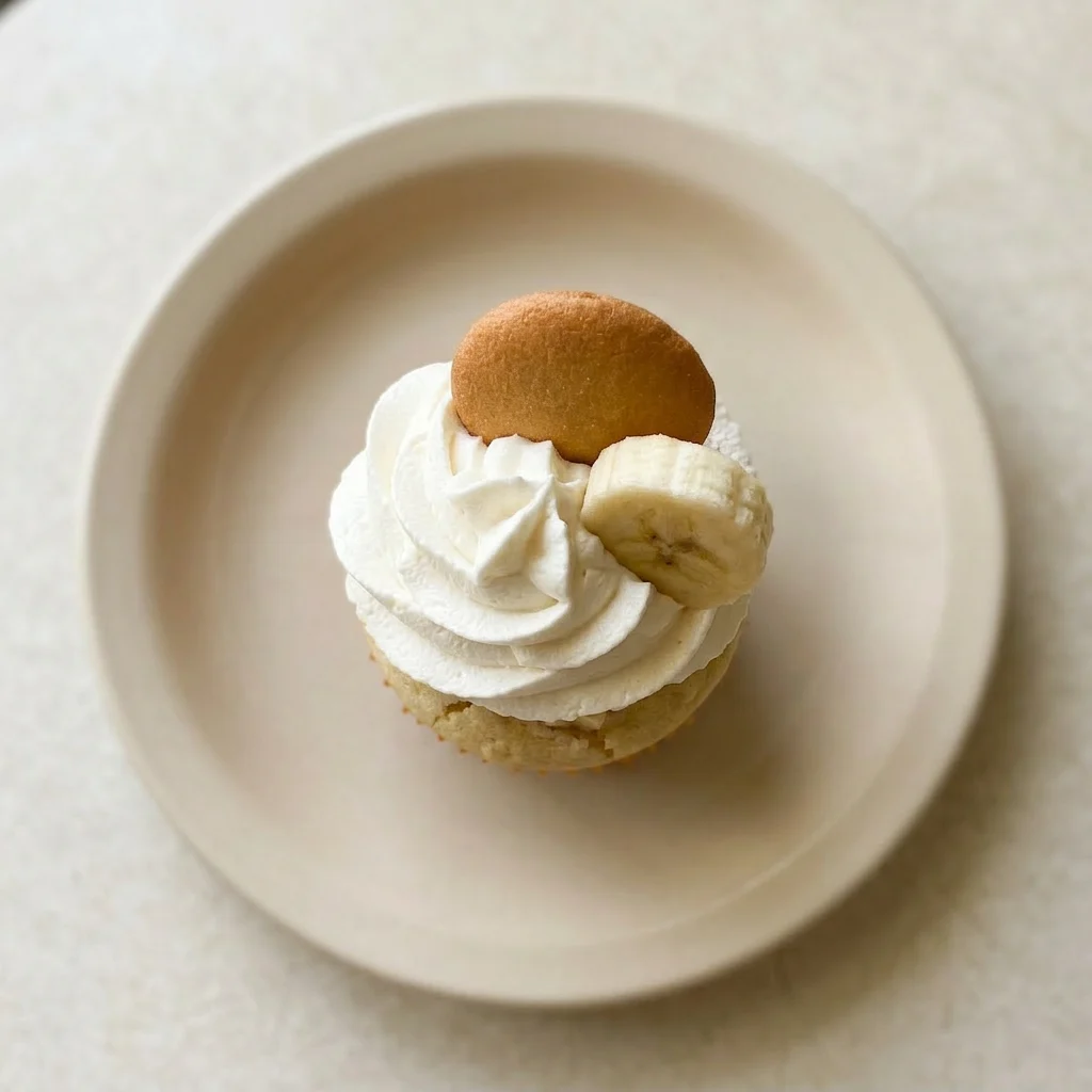 A serving of banana pudding cupcake with banana, whipped cream, and vanilla wafer garnish.