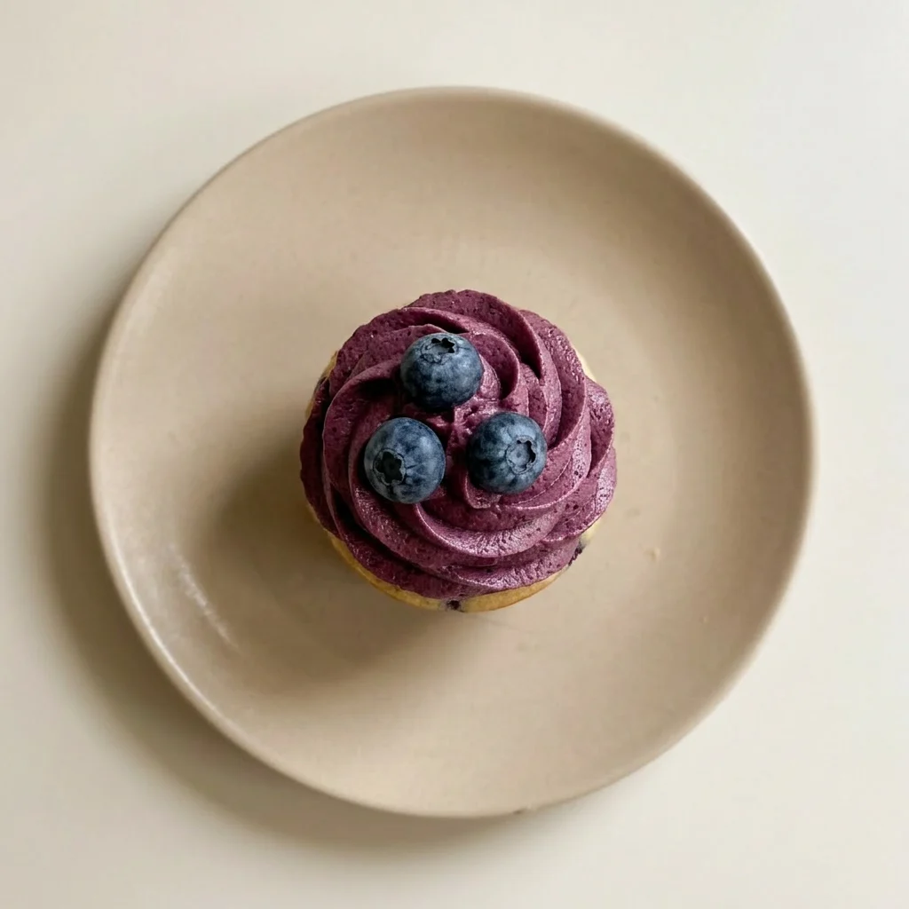 A plate of blueberry cupcakes with visible blueberries and vanilla buttercream, garnished with lemon zest.