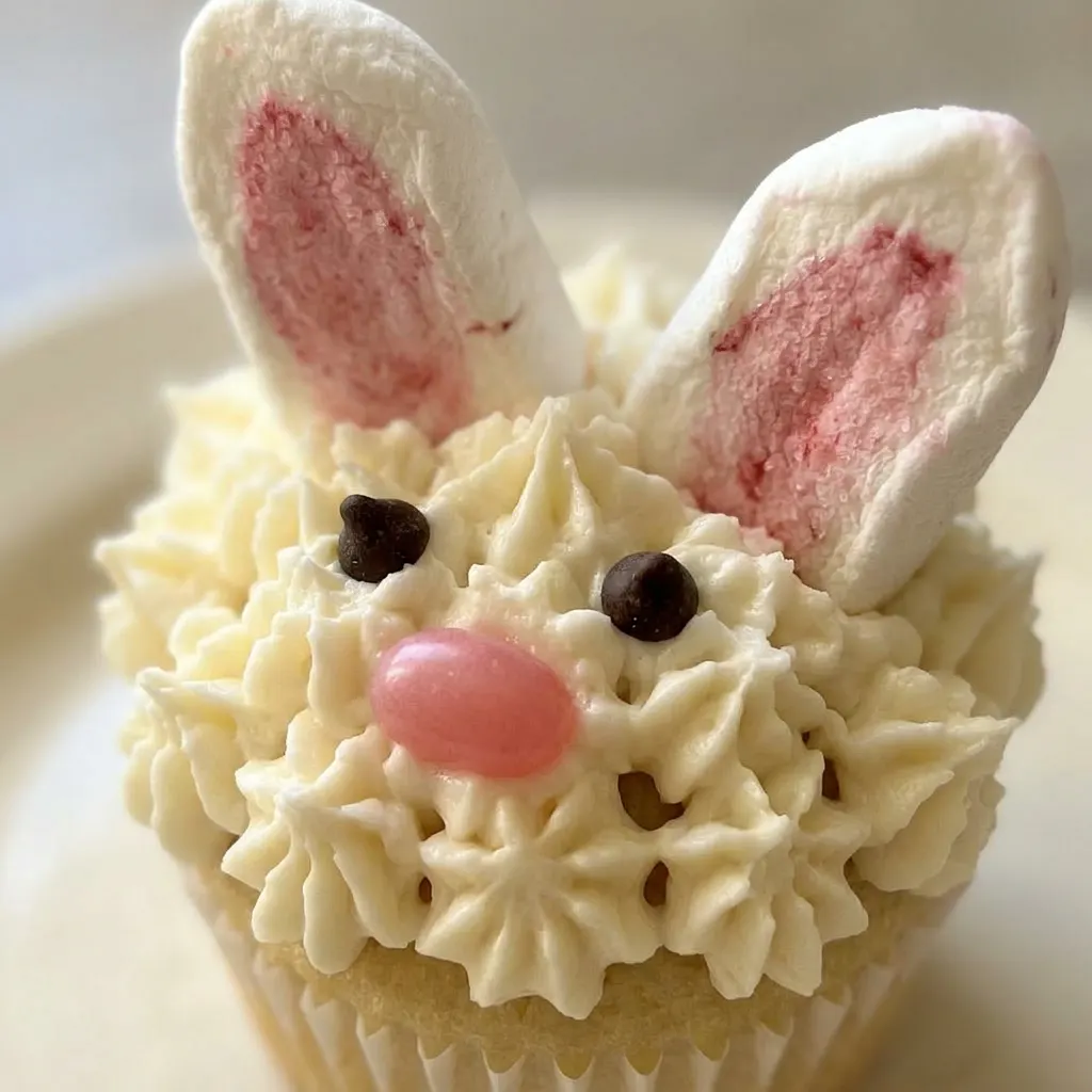 Macro detail of a bunny cupcake showing marshmallow ears, shredded coconut, and chocolate chip eyes.