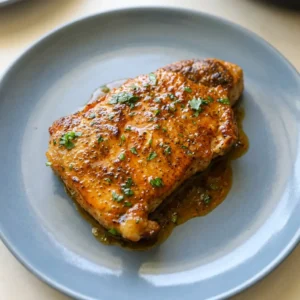 Looking down at two pork chops topped with lemon slices and melted butter, sprinkled with Cajun seasoning.