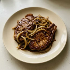 Overhead shot of two pork chops glazed with dark soy sauce, topped with sliced green onions and fried shallots on a bed of caramelized onions.