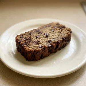 Top-down look at a slice of chocolate chip banana bread on a white surface, showing banana chunks and chocolate chips scattered throughout the crumb.