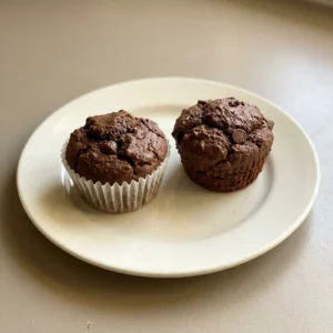 Looking down at three chocolate muffins topped with chocolate chips on a white plate.
