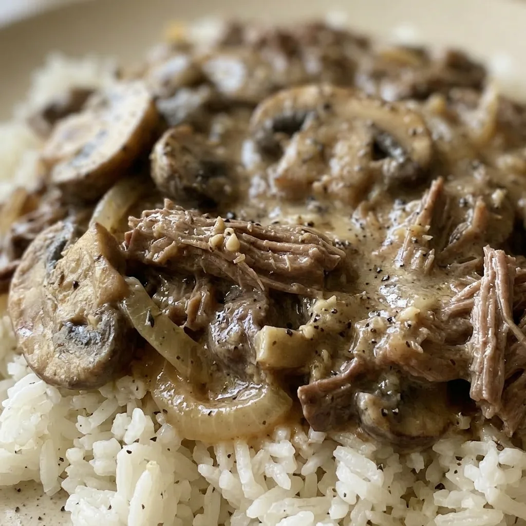 Zoomed in on a forkful of egg noodles and beef stroganoff, with visible sour cream swirls and mushroom slices.