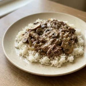 Bird's-eye view of egg noodles topped with beef stroganoff, featuring beef chunks, mushrooms, and onion in a creamy sauce.
