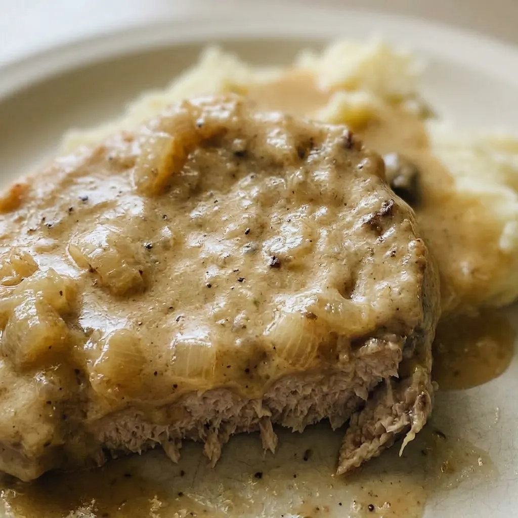 Zoomed in on a pork chop with creamy mushroom gravy and onion slices.