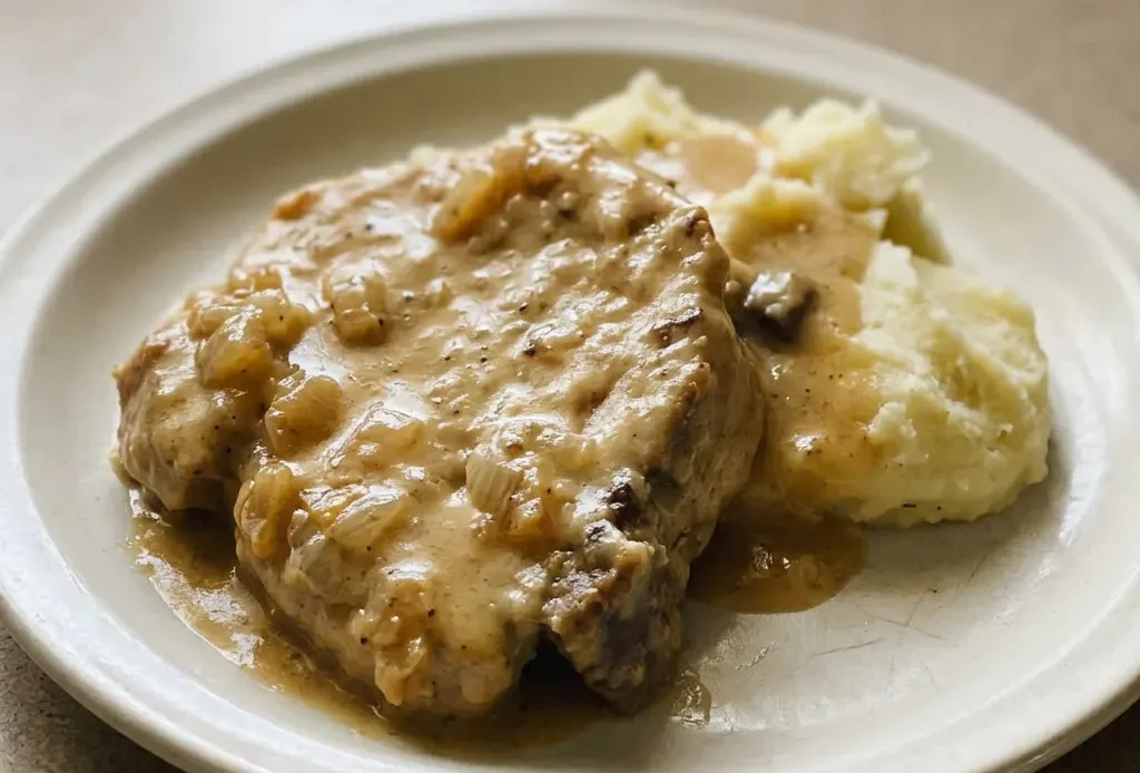 Bird's-eye view of two pork chops in thick gravy with sliced onions on top.