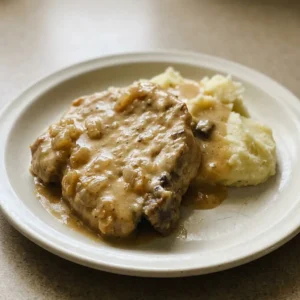 Bird's-eye view of two pork chops in thick gravy with sliced onions on top.