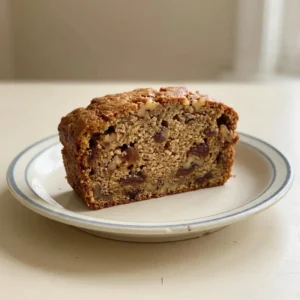 Looking down at a slice of date nut bread with visible walnut pieces and date chunks, topped with a pat of butter.