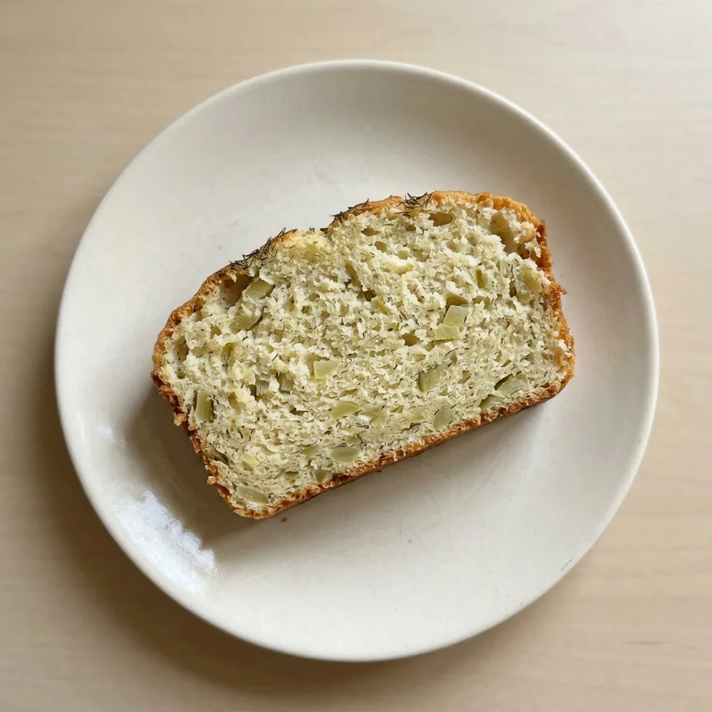A plate of bread slices with visible pickle pieces and dried dill on the crust.
