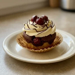Bird's-eye view of a dark chocolate muffin topped with a swirl of chocolate cream and a single sour cherry.
