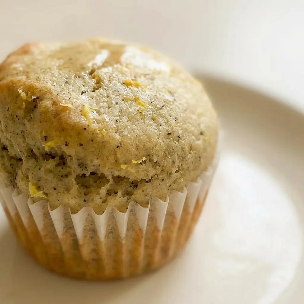 Close view of a muffin's golden-brown top, showing a honey glaze, a thin lemon slice, and small flecks of Earl Grey tea.