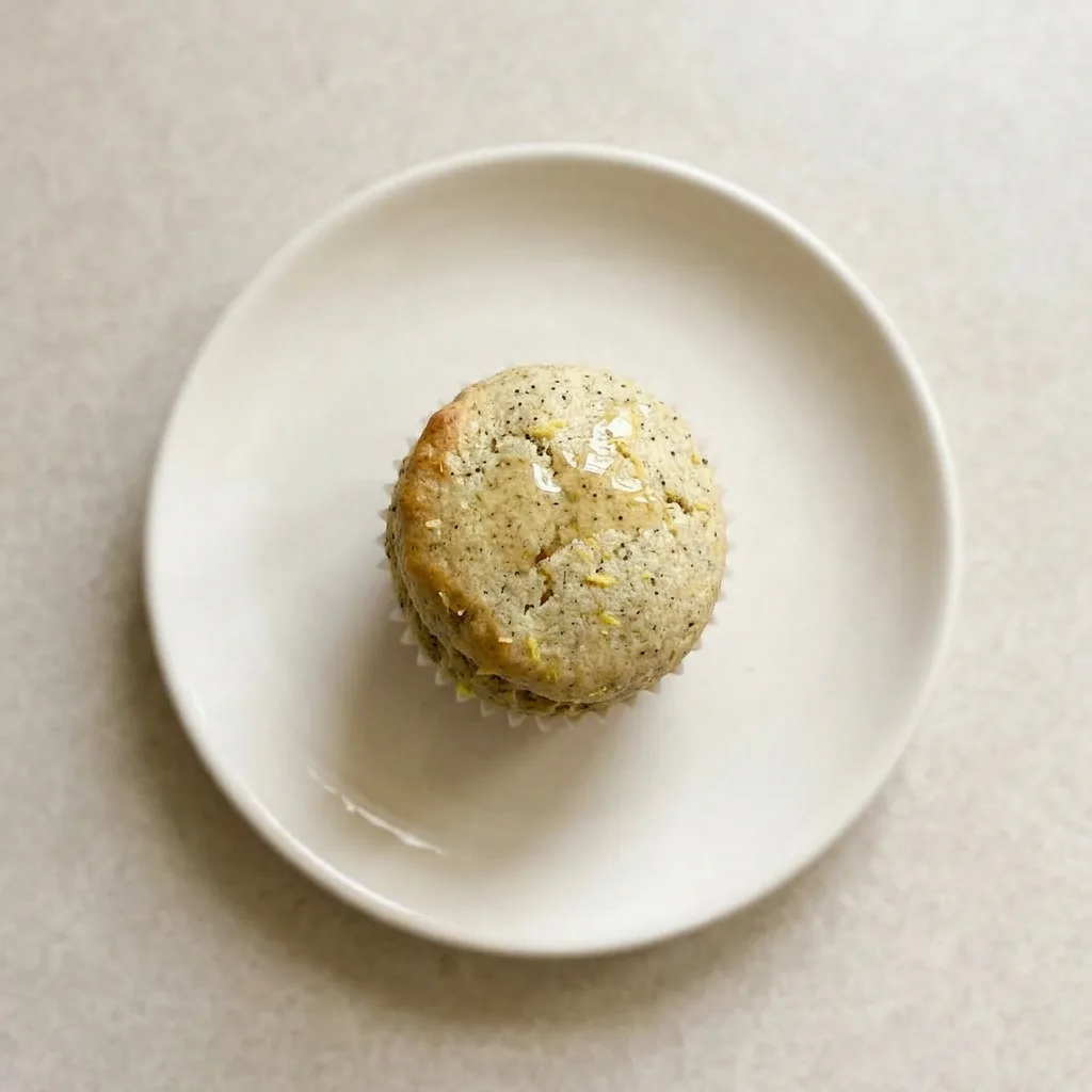Plated muffin on a white surface, its top glistening with honey, garnished with a lemon curl and a sprinkle of tea leaves.