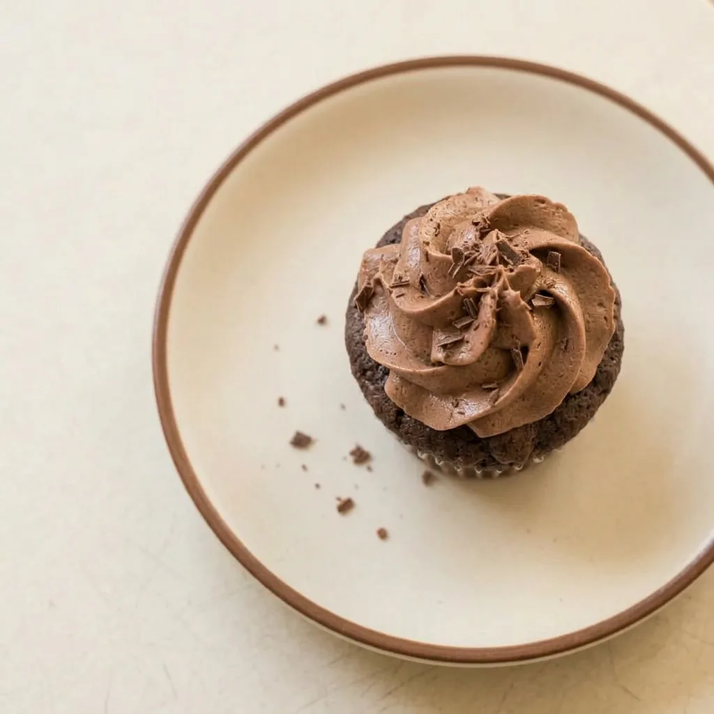 Plated chocolate cupcake topped with devil's food cake crumbles and a drizzle of chocolate sauce.