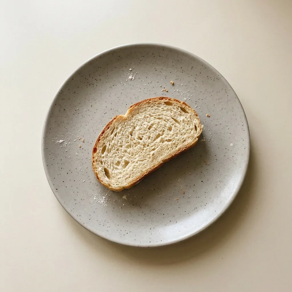 Plated bread loaf on a wooden board, sliced, with olive oil and yeast visible on the crust.