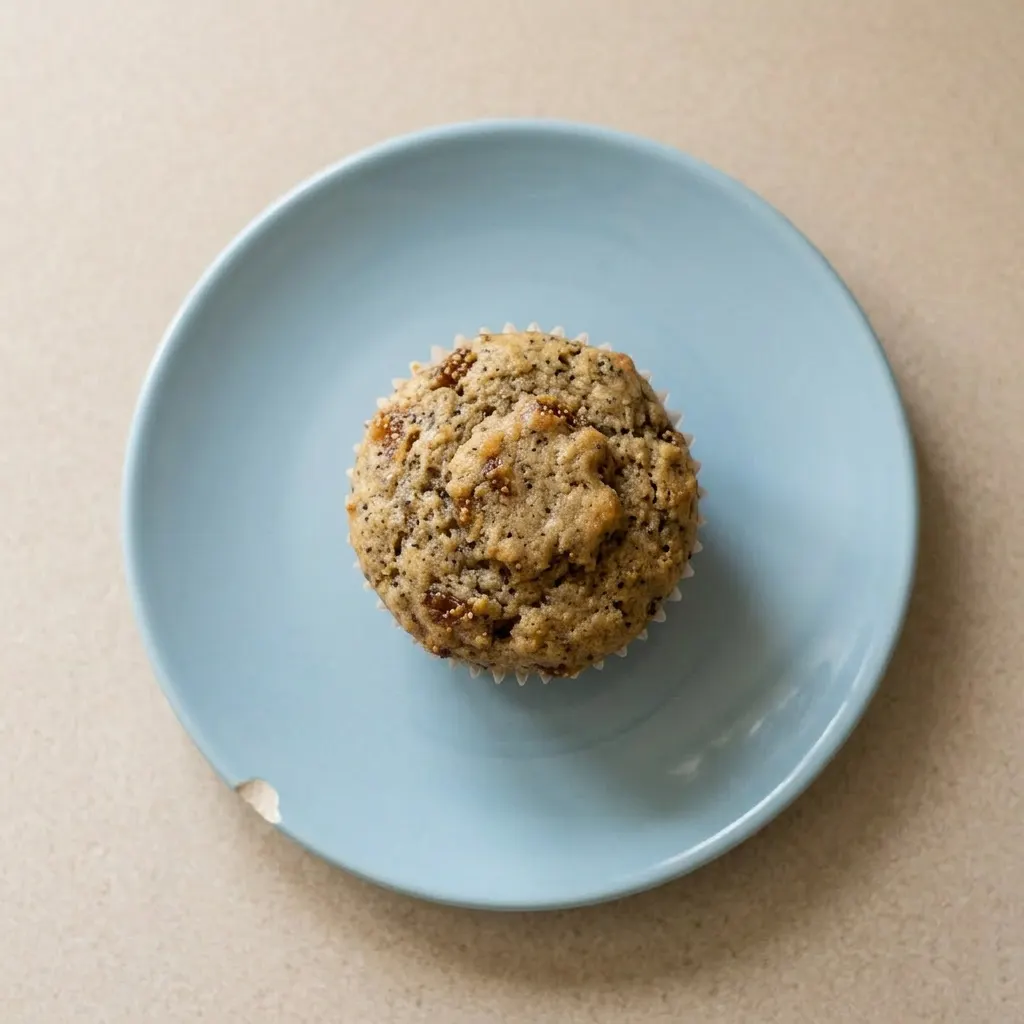 A plate of two fig muffins, one halved to show moist interior with fig chunks, topped with butter and cinnamon.