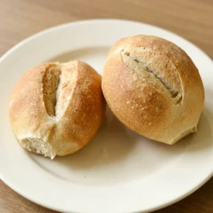 Overhead shot of two round bread rolls with a golden-brown crust and diagonal slashes, one topped with butter pats.