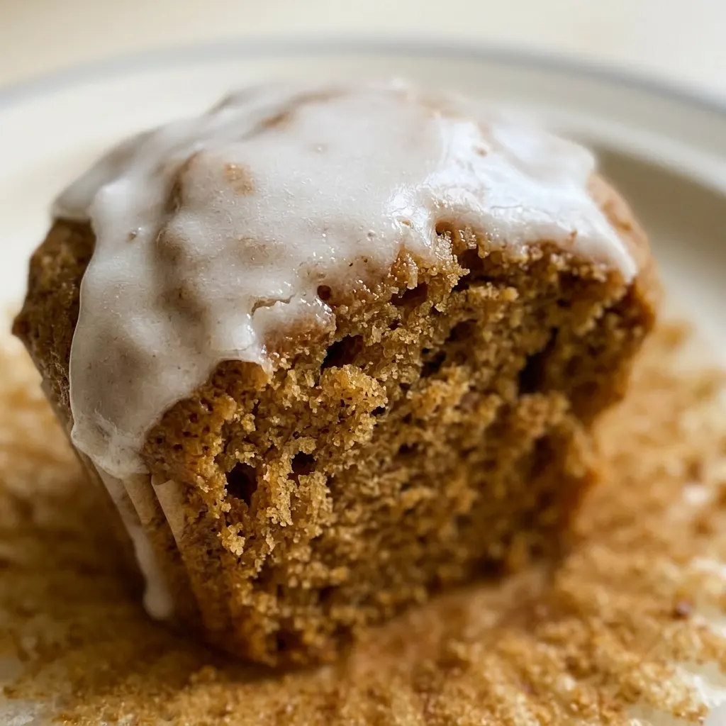 Close view of a gingerbread muffin with a glossy white glaze, visible cinnamon and ginger specks, and a cream drizzle.