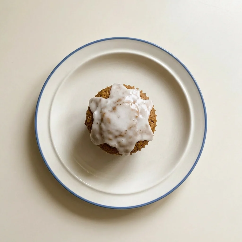 Plated gingerbread muffin with a smooth white glaze and a light cream drizzle, seen from a low angle.