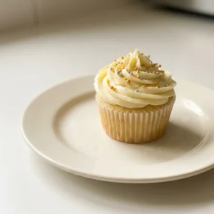 Top-down look at vanilla cupcakes with buttercream frosting and colorful sprinkles.