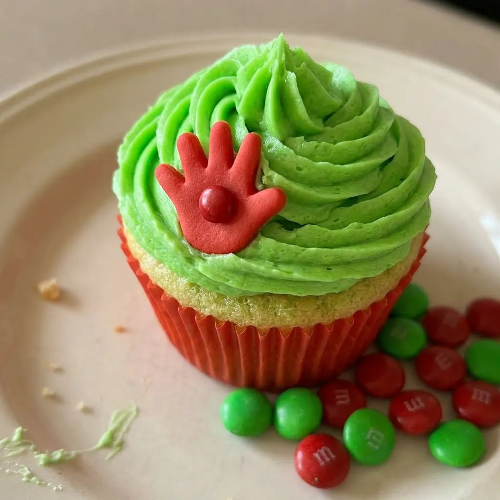 Close view of a green cupcake with white frosting and a red M&M on top, showing the cake crumb.