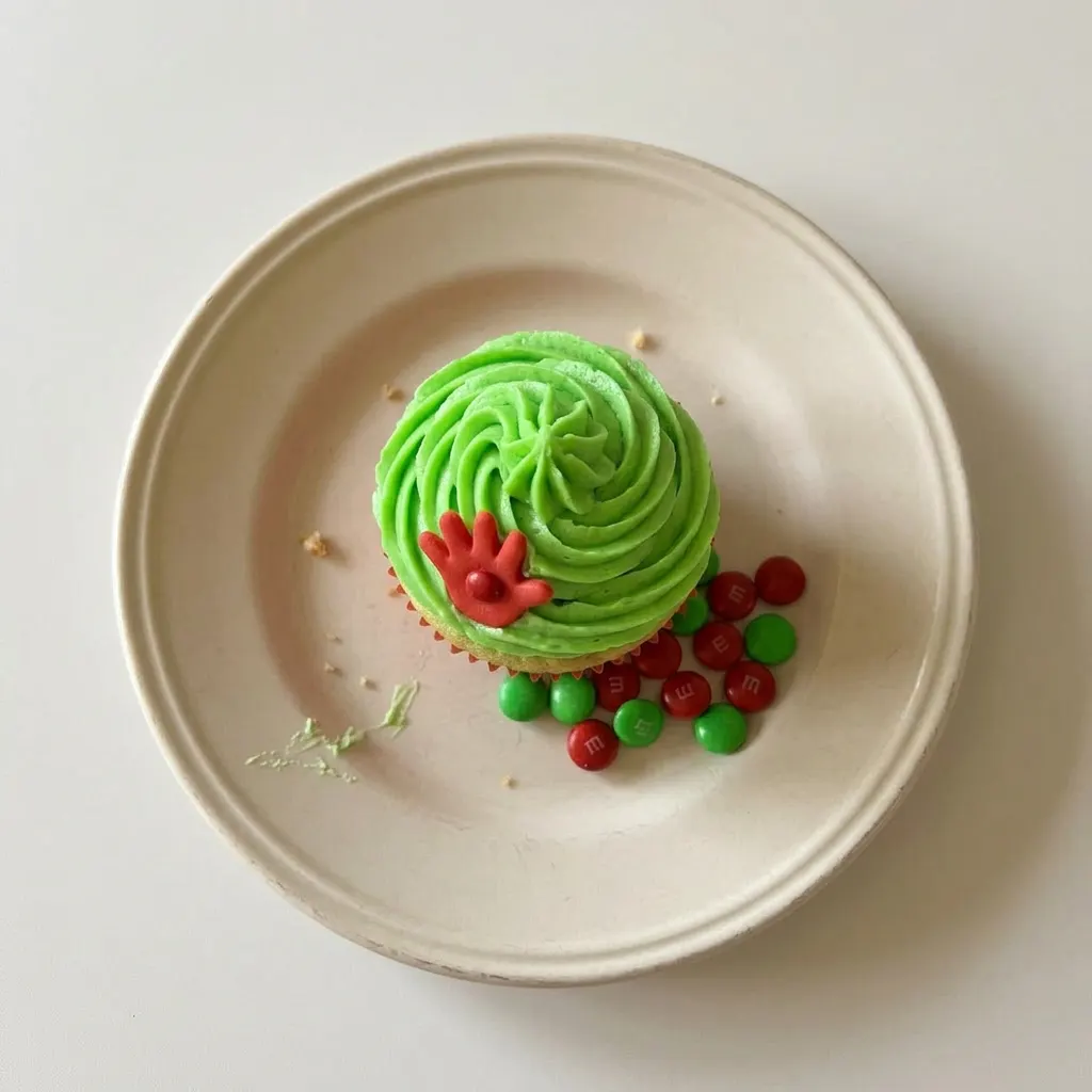 Plated green cupcakes with white frosting and red M&Ms, arranged in a row.