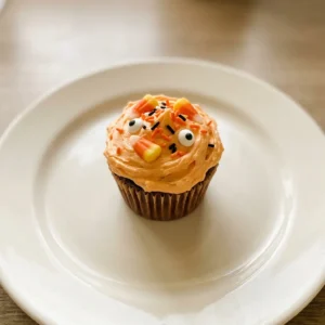 Bird's-eye view of a board with chocolate and vanilla cupcakes topped with matching buttercream, candy corn, chocolate chips, sprinkles, and candy eyes.