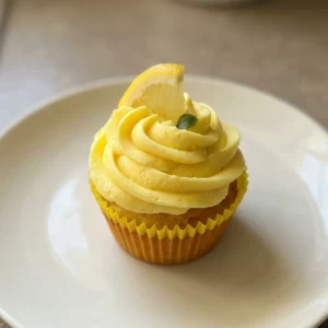 Overhead shot of a lemon cheesecake cupcake with cream cheese frosting, lemon slice, and white sprinkles.