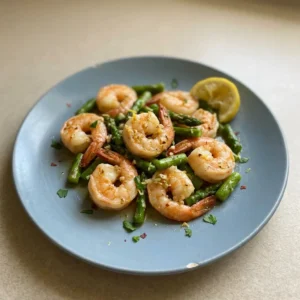 Top-down look at grilled shrimp and asparagus spears with garlic slices and lemon wedges.