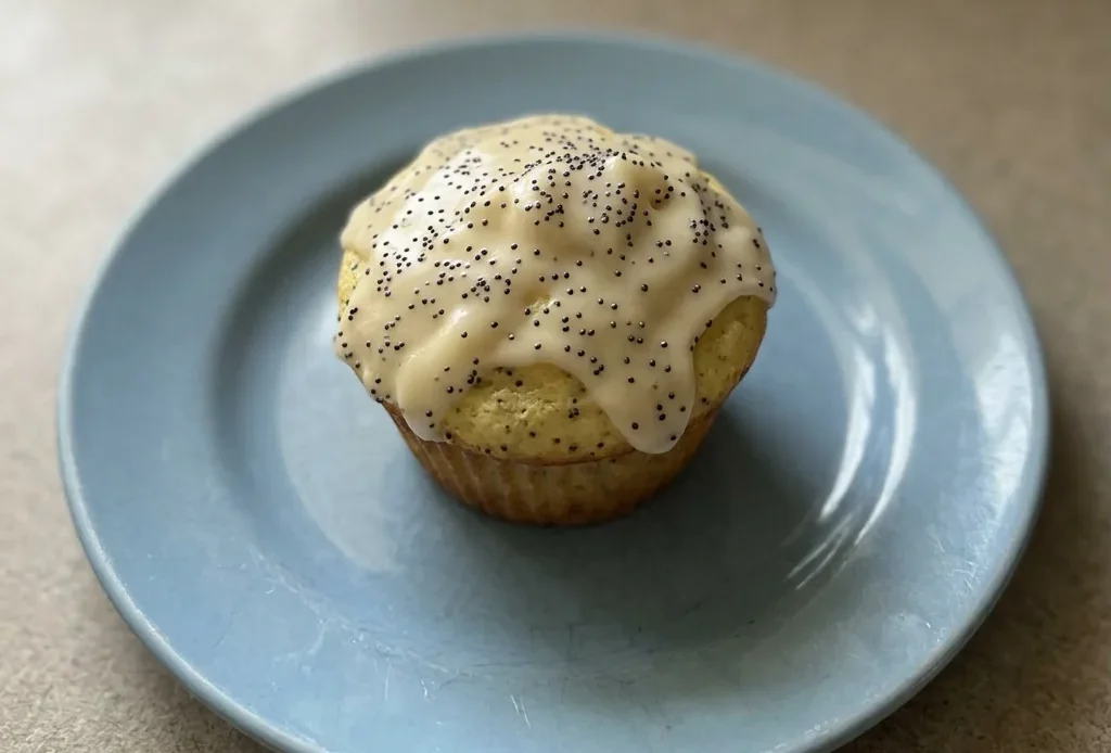 Overhead shot of a lemon poppy seed muffin topped with powdered sugar, showing a golden-brown dome with visible poppy seeds.
