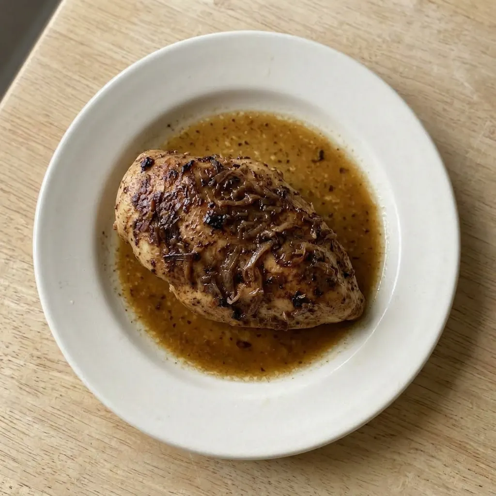 A plate of golden-brown chicken pieces in a savory broth, topped with softened onion flakes.